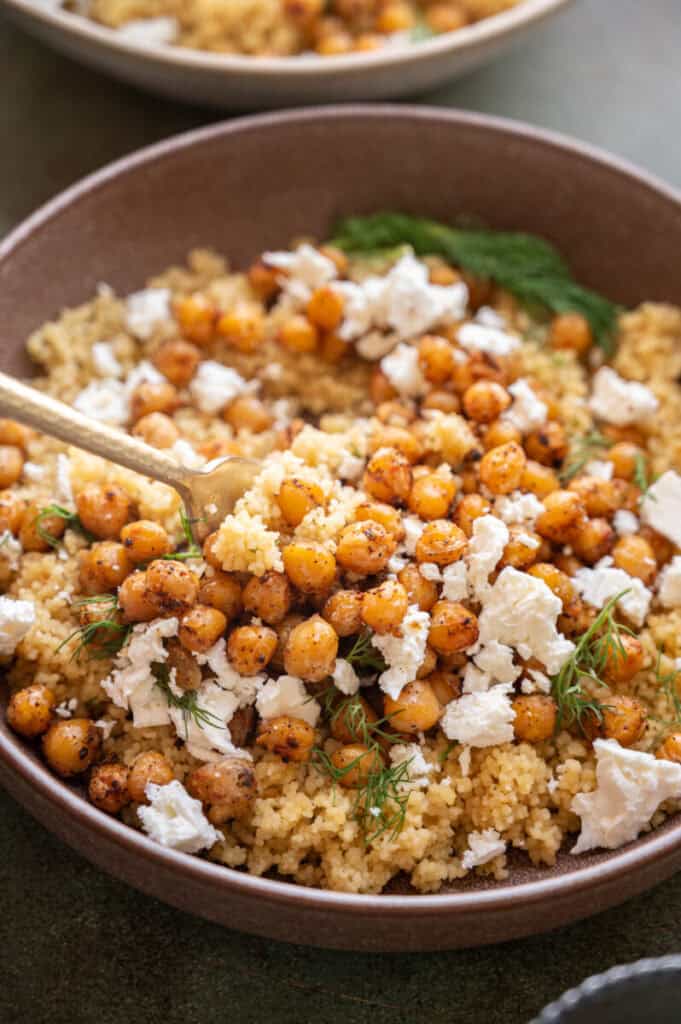 fork digging into couscous, chickpeas, and feta with dill.