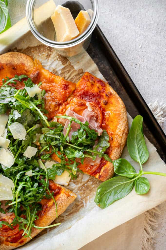 arugula pizza with prosciutto on a baking tray.