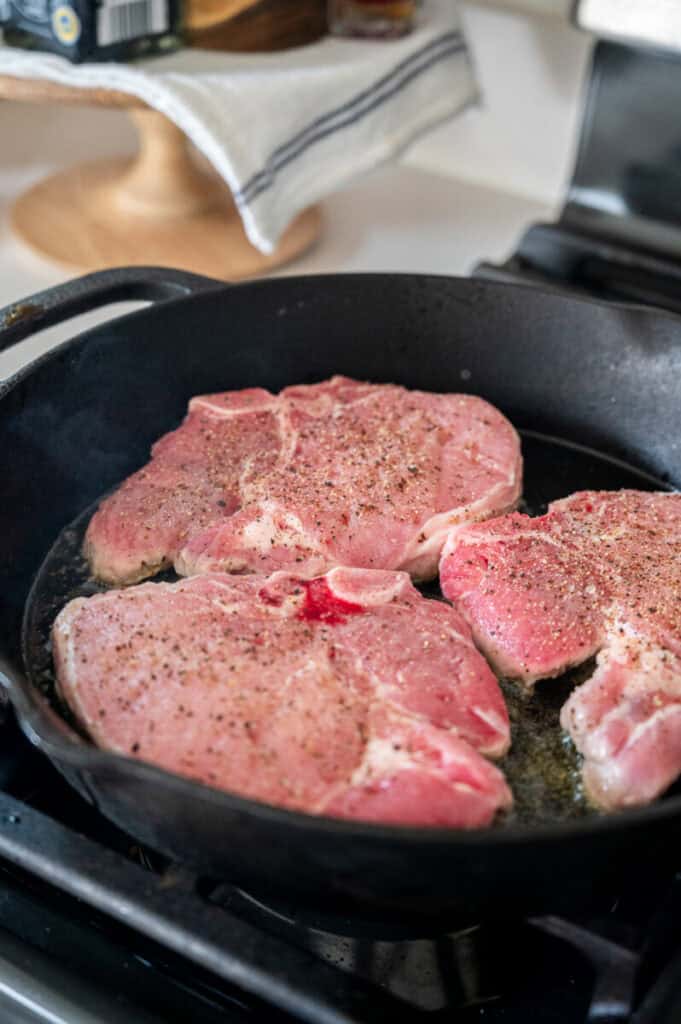 pork chops searing in a skillet.