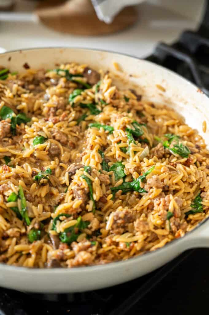 One pot sausage and spinach orzo in a skillet.