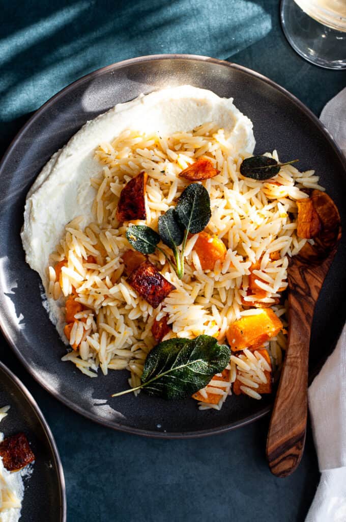 Orzo, butternut squash, sage, and a wooden spoon in a bowl