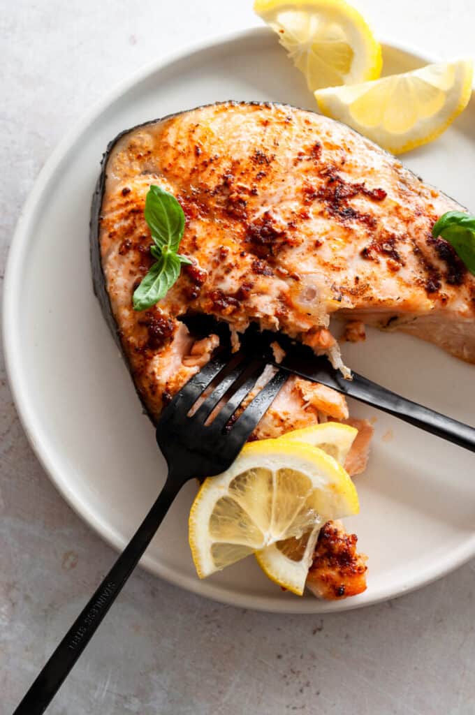 fork and knife cutting into baked salmon steak