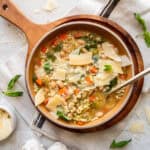 Cannellini Bean and Escarole Soup in a orange bowl with a gold spoon