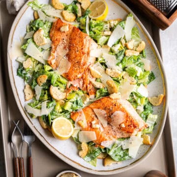 salmon caesar salad on a tray with forks and croutons
