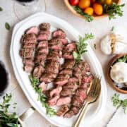 sliced lamb tenderloin on a white plate with herbs