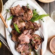 seared lamb chops on a serving tray with fresh herbs.