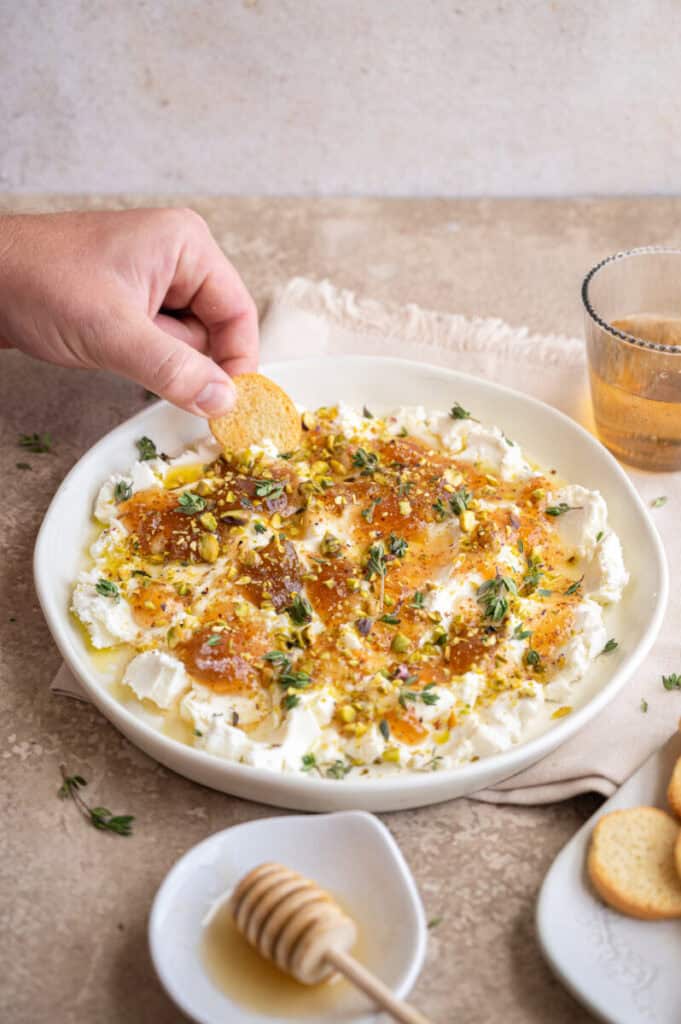hand scooping a cracker in goat cheese appetizer.