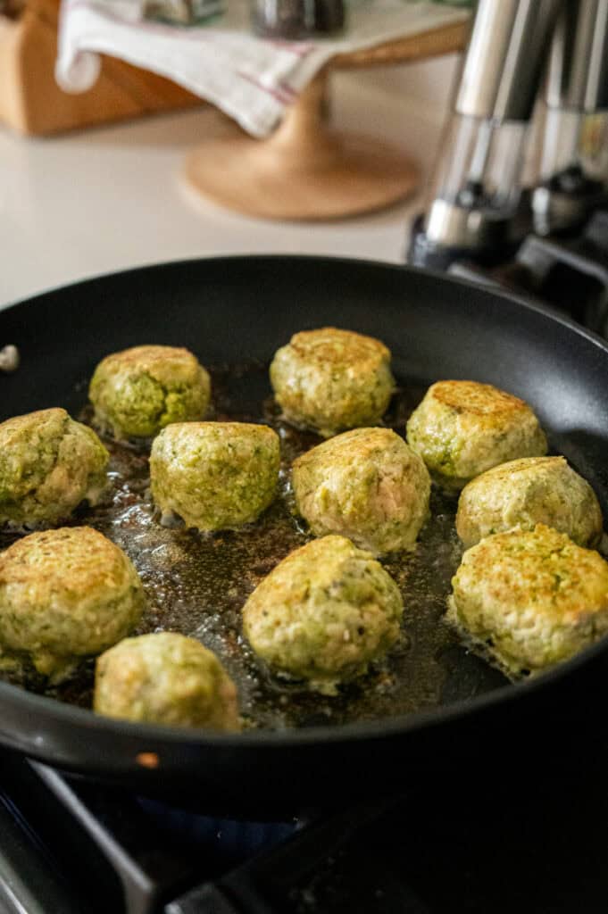 pesto chicken meatballs searing in a pan.